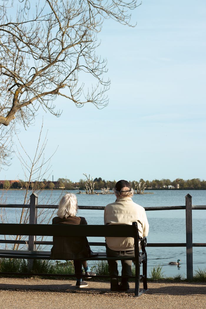 A senior couple sits on a bench by a tranquil lake on a sunny spring day.