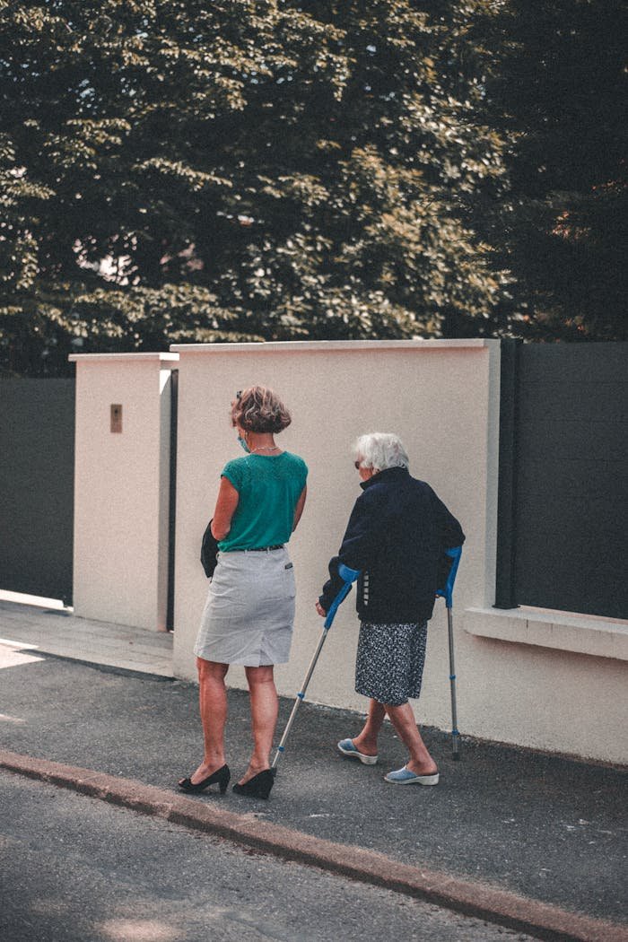 Senior woman with crutches walking alongside a companion on a sunny day in Lyon, France.