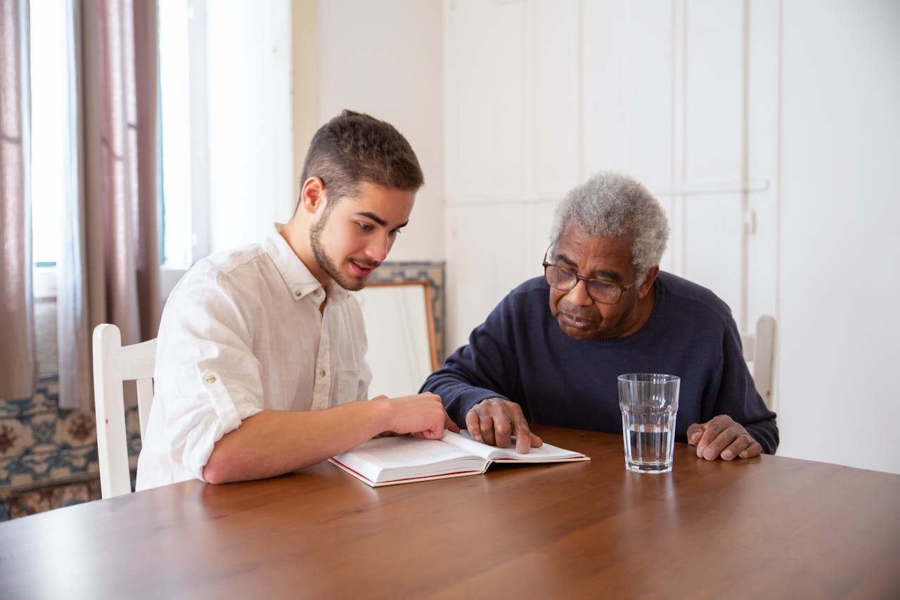 A young man and senior sharing a book, fostering connection and learning.